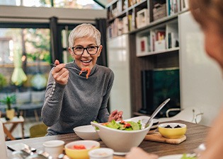Woman with black glasses smiling while eating with friend