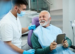 Senior patient looking at dentist while holding small mirror