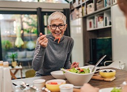 Woman with black glasses smiling while eating with friend