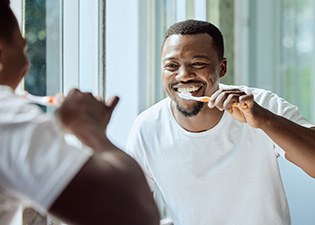 Man smiling while brushing his teeth in bathroom