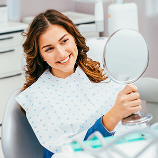 Young woman examining smile in dental office