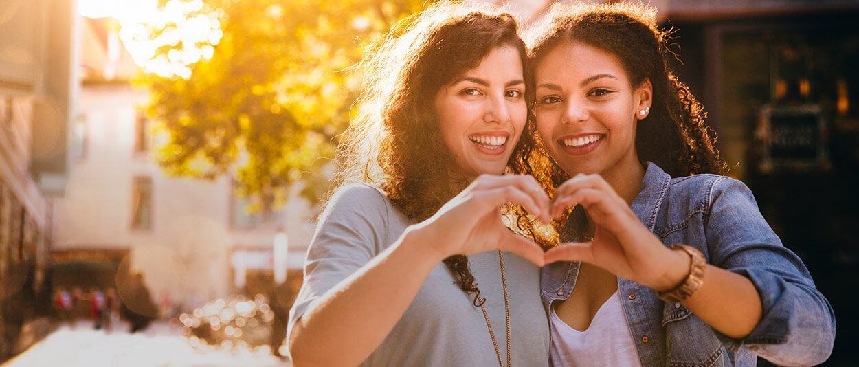 Two women smiling making heart with hands