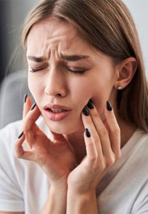 a woman experiencing tooth pain and touching her cheeks