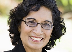 An older woman wearing glasses and a business suit smiling after receiving her new smile thanks to a dental implant dentist in Marlton